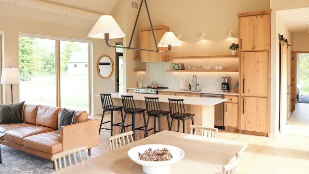 Una cocina moderna con armarios de madera, una isla central y taburetes de bar. Hay una mesa de comedor con un bol de aperitivos.