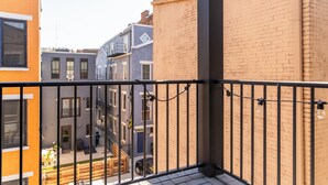 A balcony with a view of neighboring buildings, a wooden bench, and a metal railing. - Cozy Downtown Loft: 2BR condo w/ AC, WiFi, Balcony & Free 2-car parking. (Cincinnati)