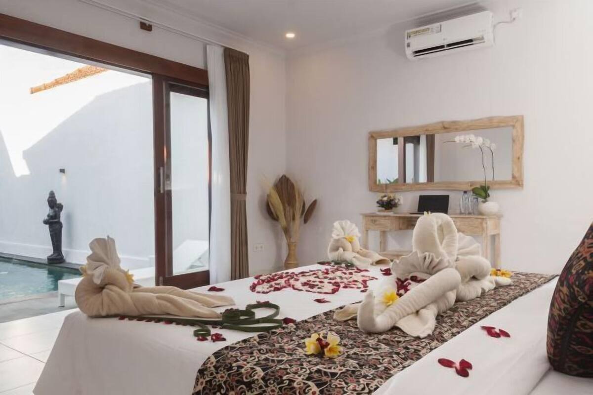 A hotel room with a bed, a desk, a mirror, and a view of a pool.