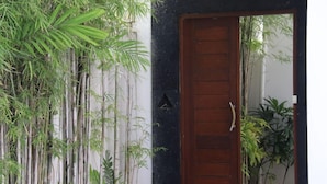 A wooden door with a simple design, a white wall with a black vertical strip, and bamboo plants surrounding the door. - Maisaba Seminyak Loft and Villas (Bali)