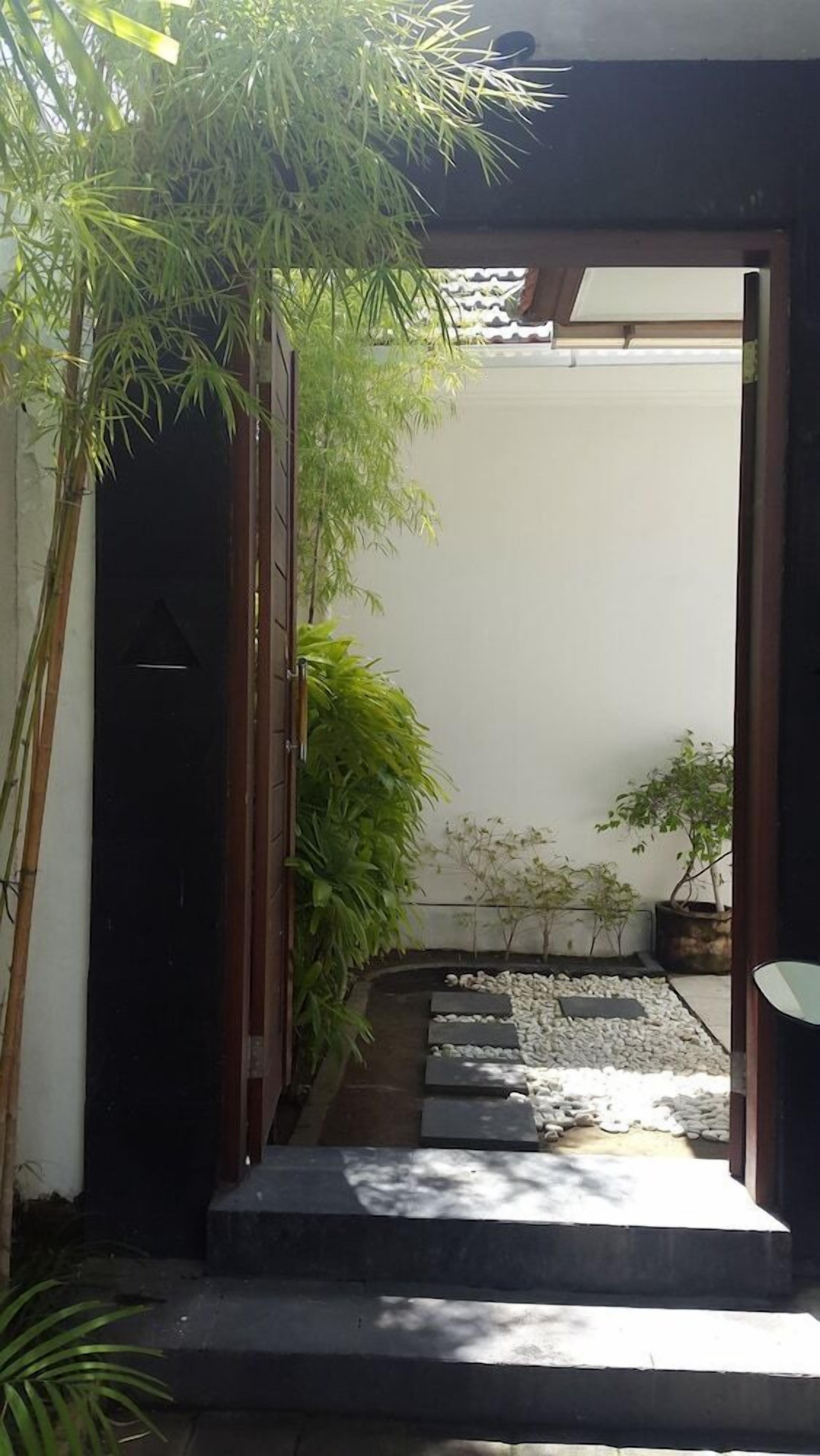 A pathway leading to a dark door, surrounded by potted plants and a small garden area.