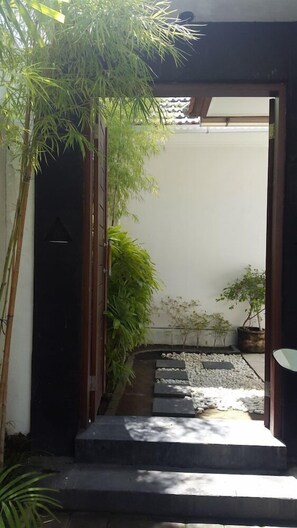 A pathway leading to a dark door, surrounded by potted plants and a small garden area. - Maisaba Seminyak Loft and Villas (Bali)