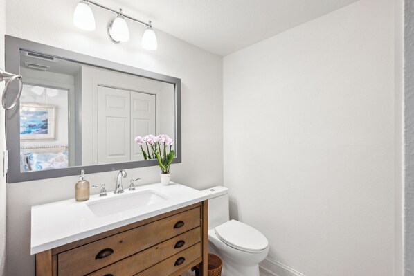 Une salle de bain avec un lavabo blanc, un meuble-lavabo en bois, un grand miroir et des toilettes.