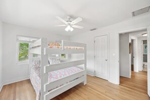Un lit superposé avec un ventilateur de plafond, des murs blancs et une fenêtre donnant sur un paysage verdoyant.
