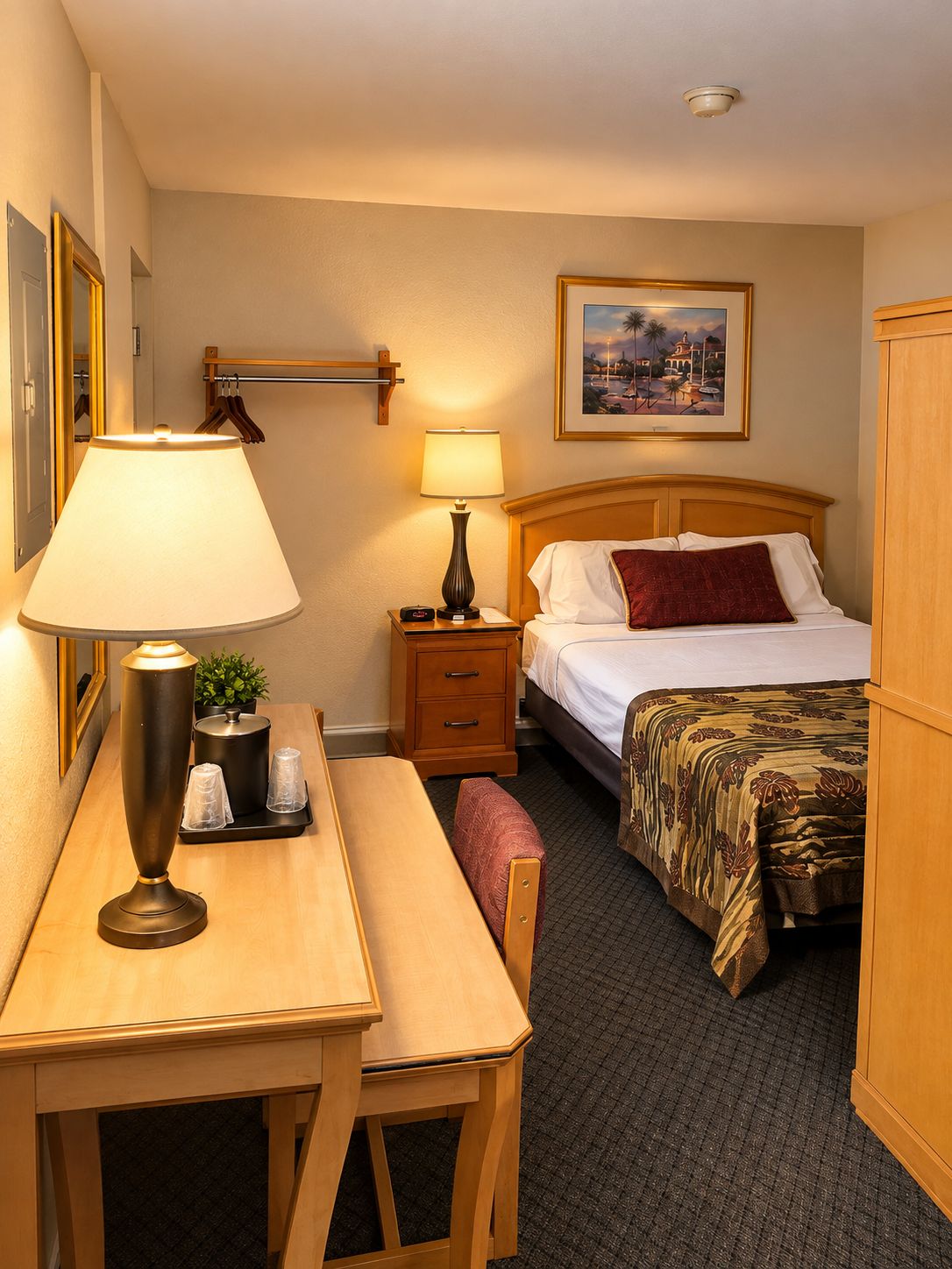 A hotel room with a bed, bedside table, lamp, and a painting on the wall.