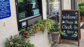 A check-in area with a sign reading "CHECK-IN" and a welcome sign. There are potted plants and a wheelchair accessibility sign. - Queens Lodge Motel (West Palm Beach)
