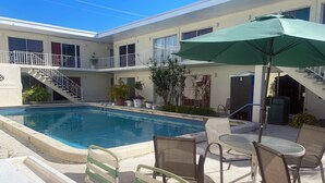 A pool area with a table and chairs, surrounded by potted plants and a staircase leading to an upper level. - Queens Lodge Motel (West Palm Beach)