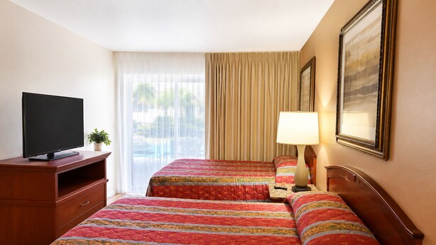 A hotel room with two beds, a TV, a lamp, and a painting on the wall. - Queens Lodge Motel (West Palm Beach)