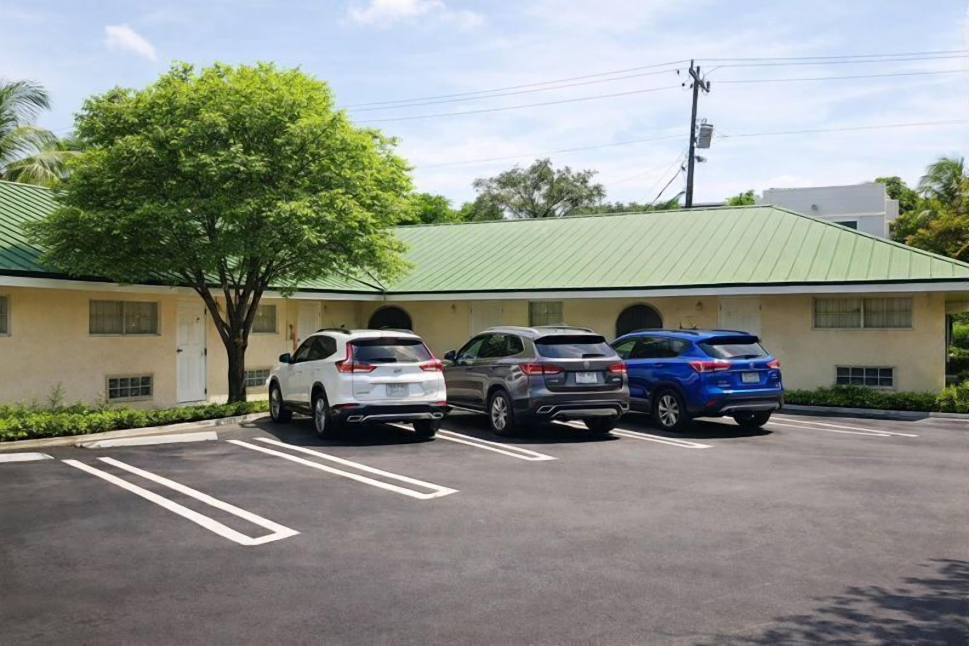 A parking lot with three cars parked in front of a building with a green roof and a tree nearby.