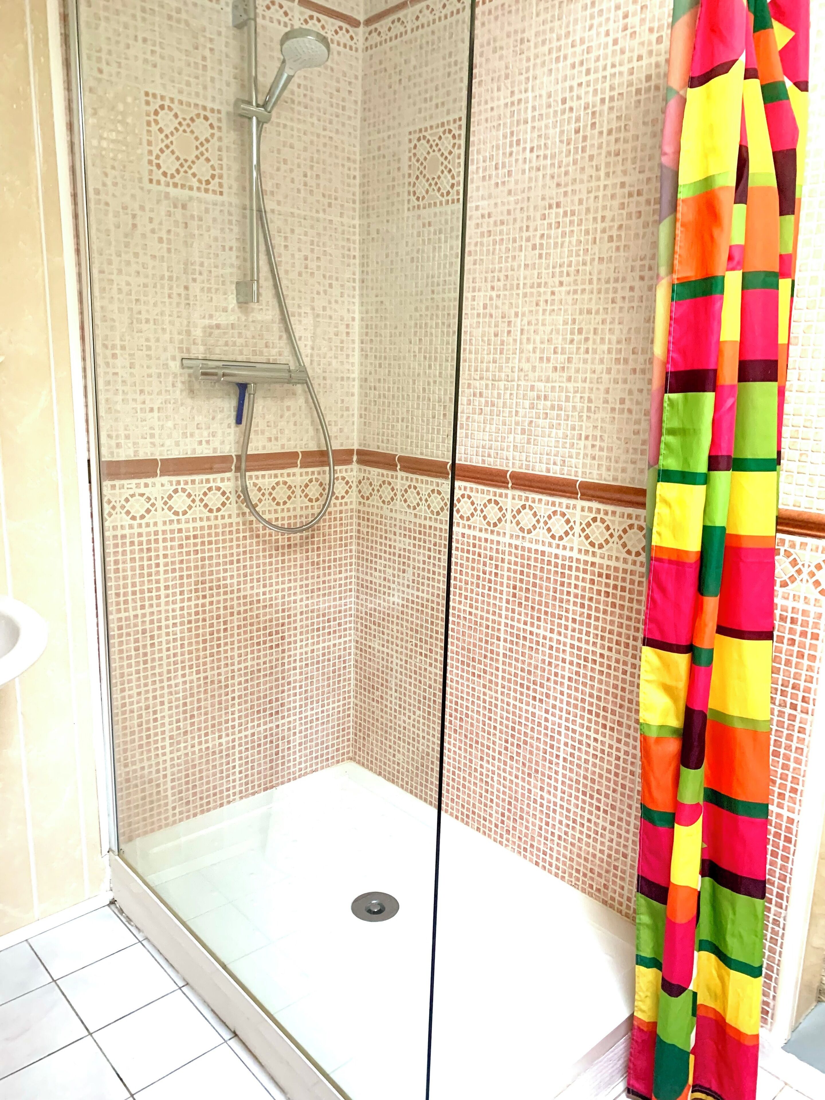 Un espace douche doté d’une porte en verre, de murs carrelés et d’un rideau de douche aux couleurs vives.