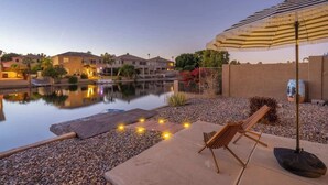 A tranquil outdoor patio with a pool, lounge chairs, and an umbrella. - Waterfront Villa with Pool Hot Tub Lounge area (Chandler)