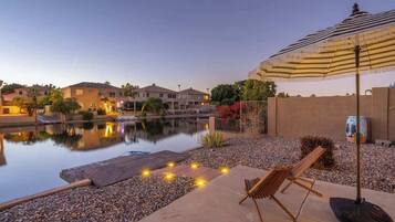 A tranquil outdoor patio with a pool, lounge chairs, and an umbrella.