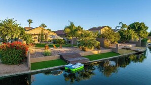 A residential area with a canal, a small boat docked at the water's edge, and houses with manicured lawns and palm trees. - Waterfront Villa with Pool Hot Tub Lounge area (Chandler)
