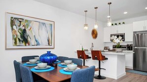 A modern kitchen with white cabinets, a stainless steel refrigerator, and a dining area with blue chairs and a wooden table.