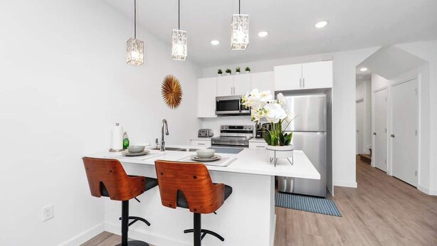 A modern kitchen with white cabinetry, a central island with bar stools, a stainless steel refrigerator, and pendant lighting.