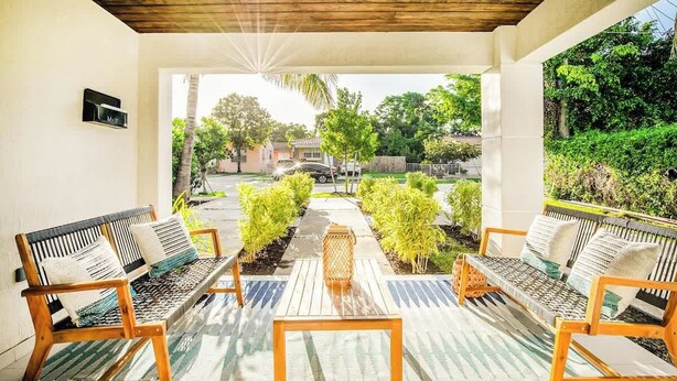 A covered outdoor seating area with wooden benches and a central table, surrounded by greenery and a view of a residential street. - 6BR Villa w/ Pool, King Beds & Top Amenities! (Miami)