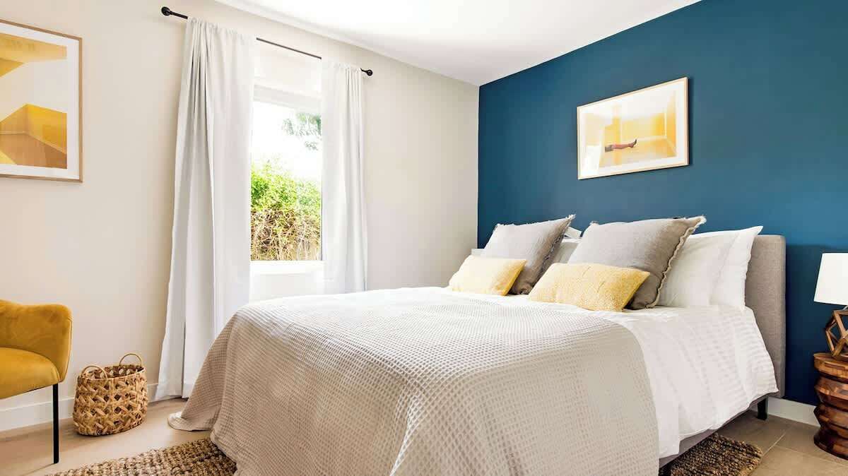 Un dormitorio con cama, una silla, una lámpara y una ventana con cortinas.