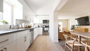 A modern kitchen with white cabinets, stainless steel appliances, and a dining area with wicker furniture. - 6BR Villa w/ Pool, King Beds & Top Amenities! (Miami)