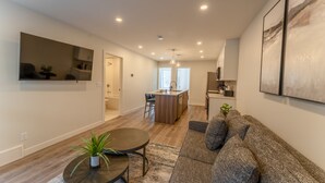 A modern living room with a sofa, a coffee table, and a TV. There is a kitchen area with a dining table and chairs. - Skyridge 401 by Canmore Premier (Harvie Heights)