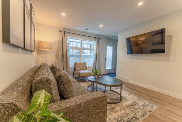 Un salon comprenant un canapé, une petite table, un fauteuil et un téléviseur fixé au mur.