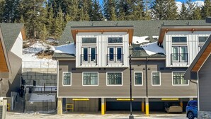 A multi-story residential building with a garage and a covered parking area. - Skyridge 401 by Canmore Premier (Harvie Heights)