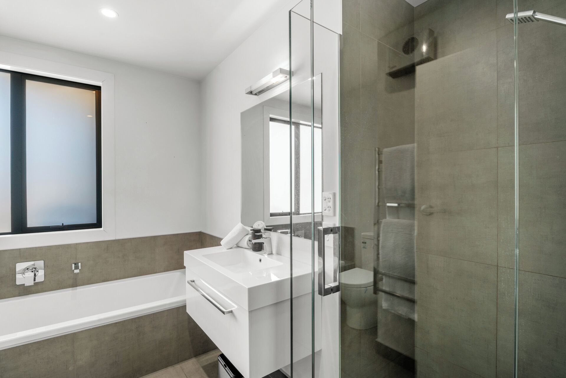Un baño moderno con ducha envuelta en vidrio, un lavabo blanco y un espejo grande.