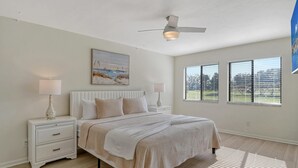 Quarto com cama, mesas de cabeceira, ventoinha no teto e janela com persianas.