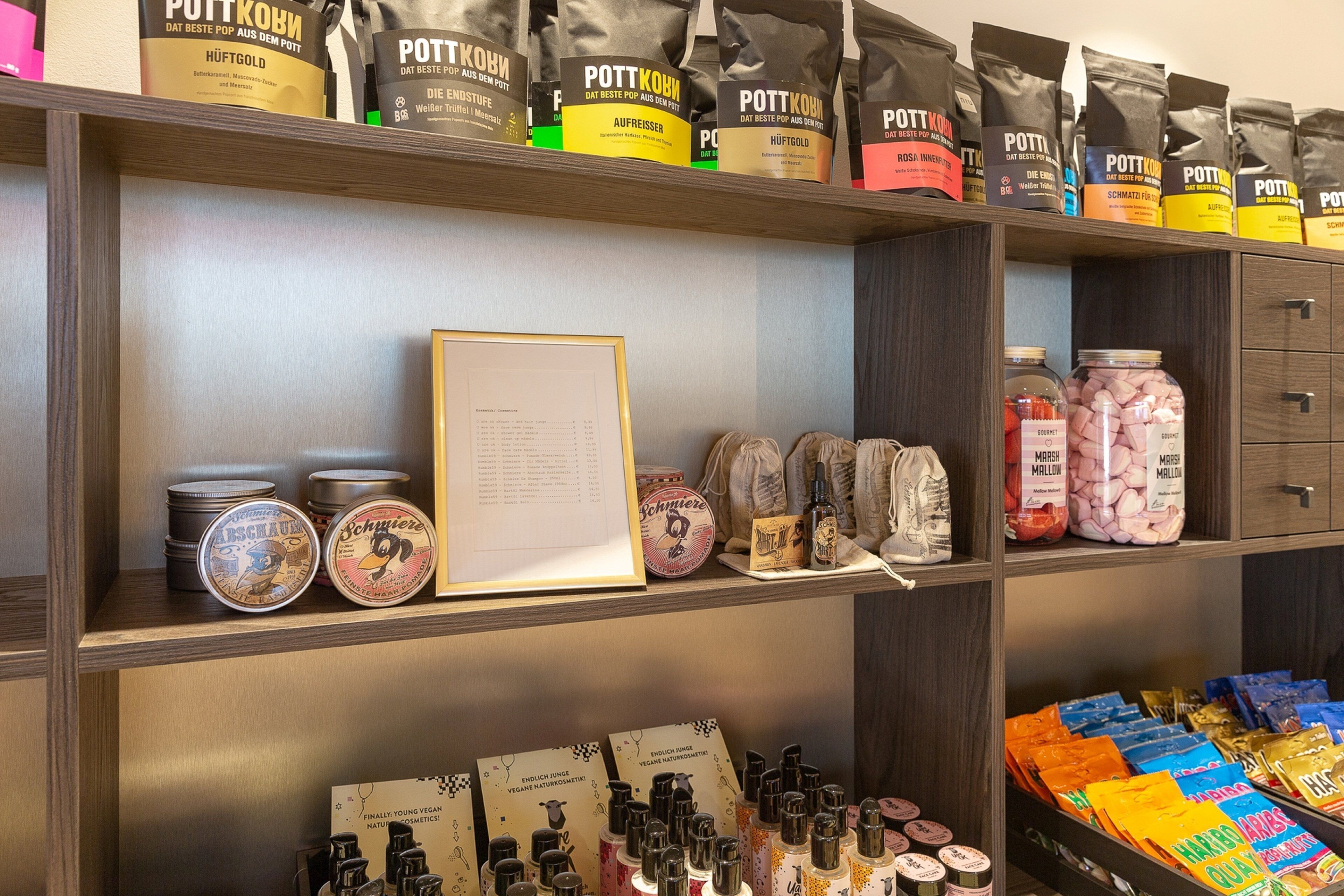 A shelf with various products including bags of Pöttkön, jars of marshmallows, and a framed menu.