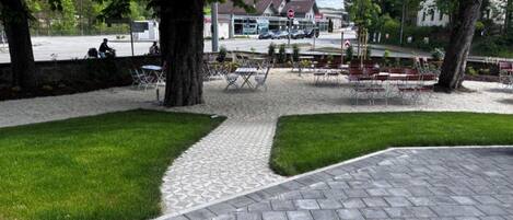 A paved outdoor area with seating, trees, and a building in the background.
