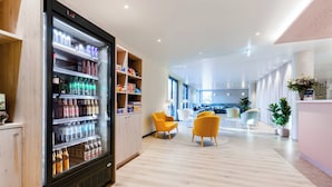 Eine moderne Hotellobby mit einer Kühlvitrine für Getränke, Holzboden und gelben Sesseln.
