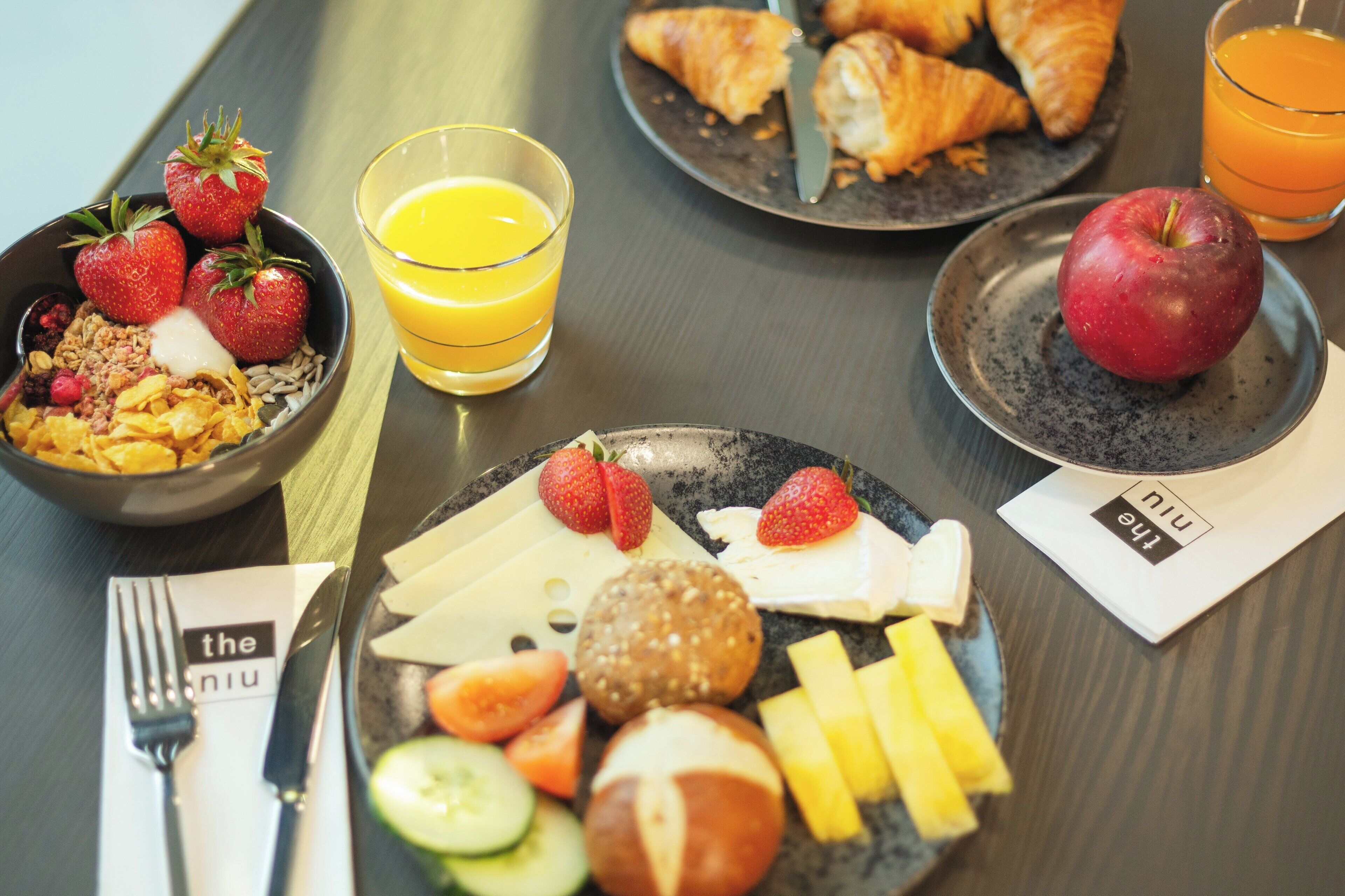 A breakfast setting with croissants, strawberries, an apple, and a glass of orange juice on a table.