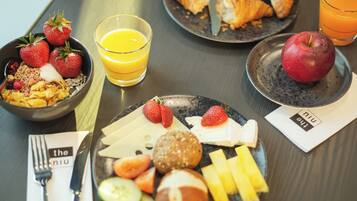 A breakfast setting with croissants, strawberries, an apple, and a glass of orange juice on a table.