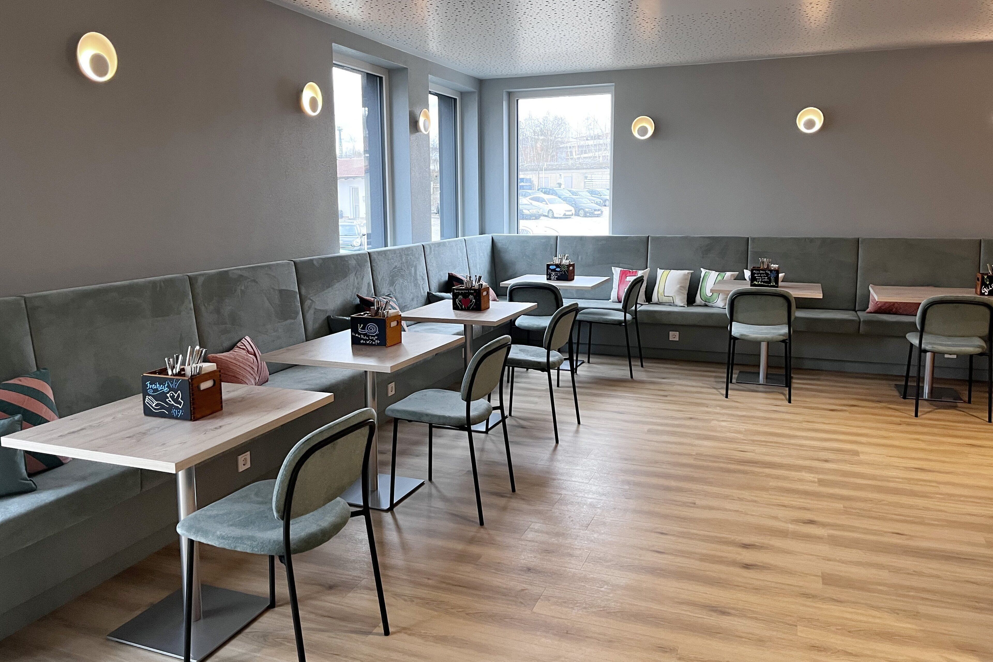 A modern cafe with grey seating, wooden tables, and natural light from large windows.