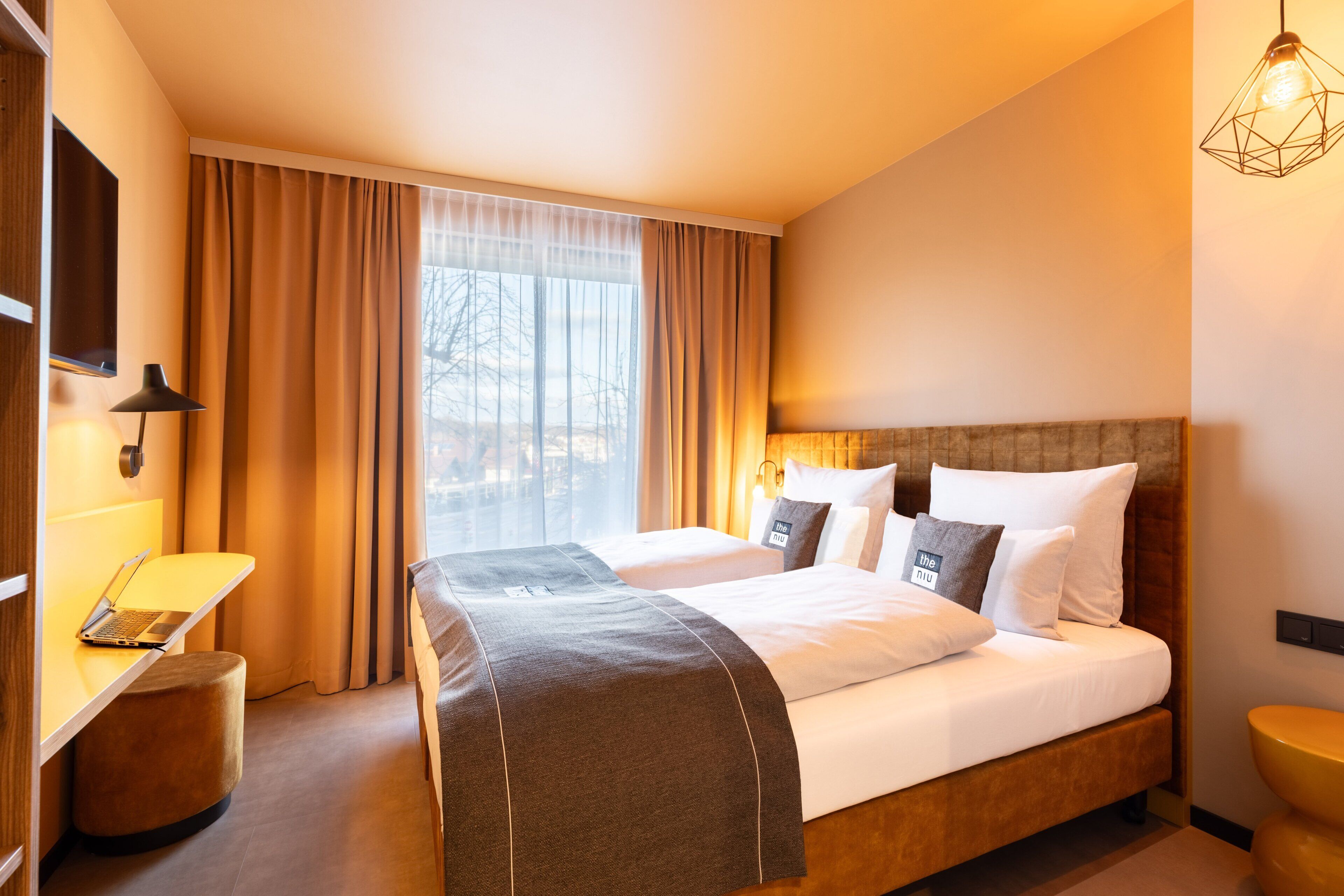 Ein Hotelzimmer mit einem großen Bett, einem Schreibtisch mit Laptop, einem Stuhl und einem Nachttisch.