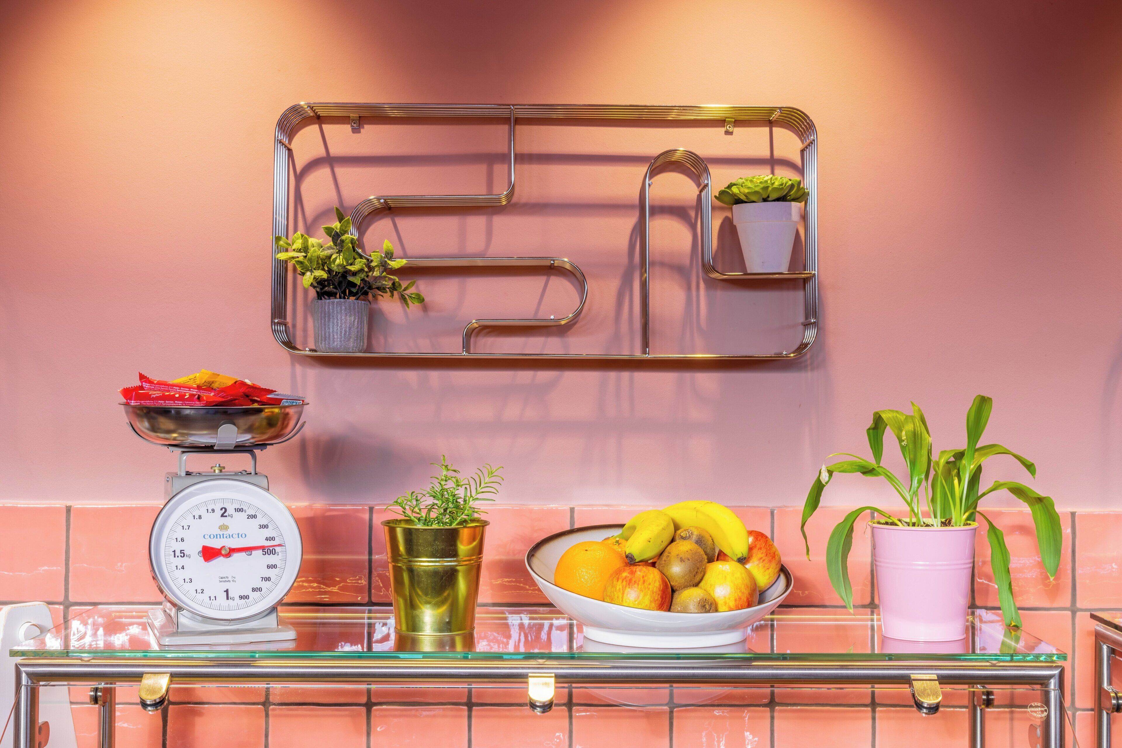 A kitchen counter with a scale, a bowl of fruit, and potted plants.