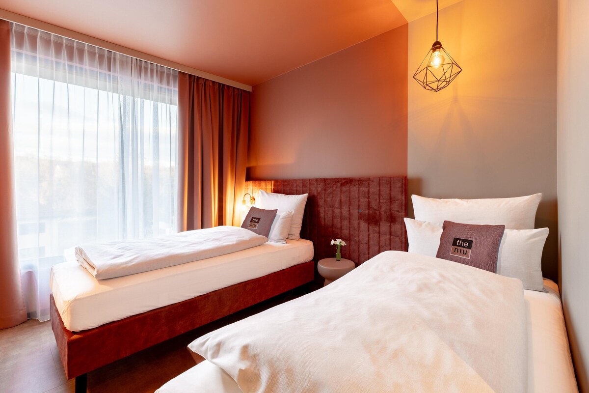 Ein Hotelzimmer mit zwei Betten, einem Holzkopfteil, einem Nachttisch mit einer Vase und einer Pendelleuchte.
