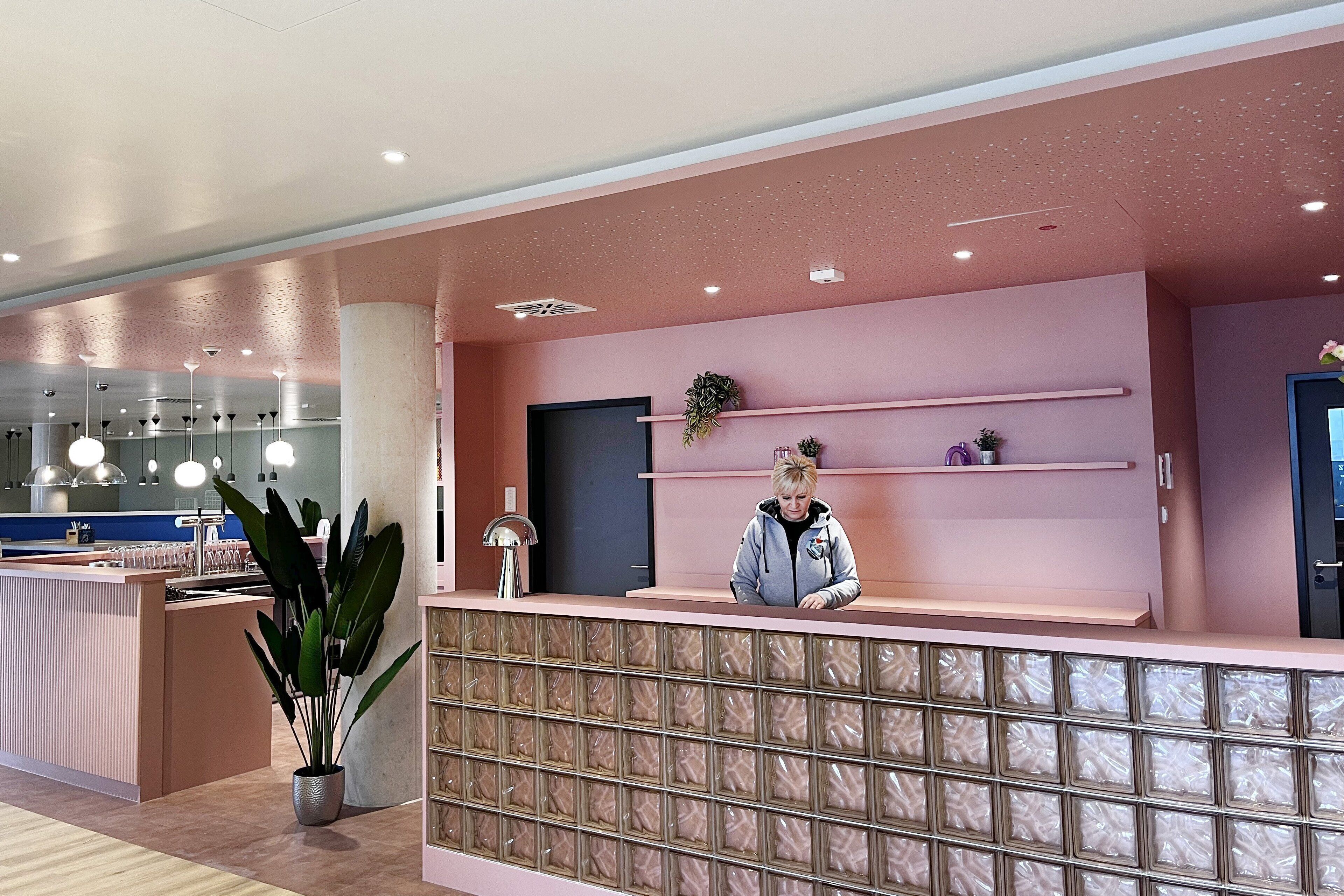 Een modern ontworpen receptiegedeelte, met een roze kleurenschema, een receptiebalie en een potplant.