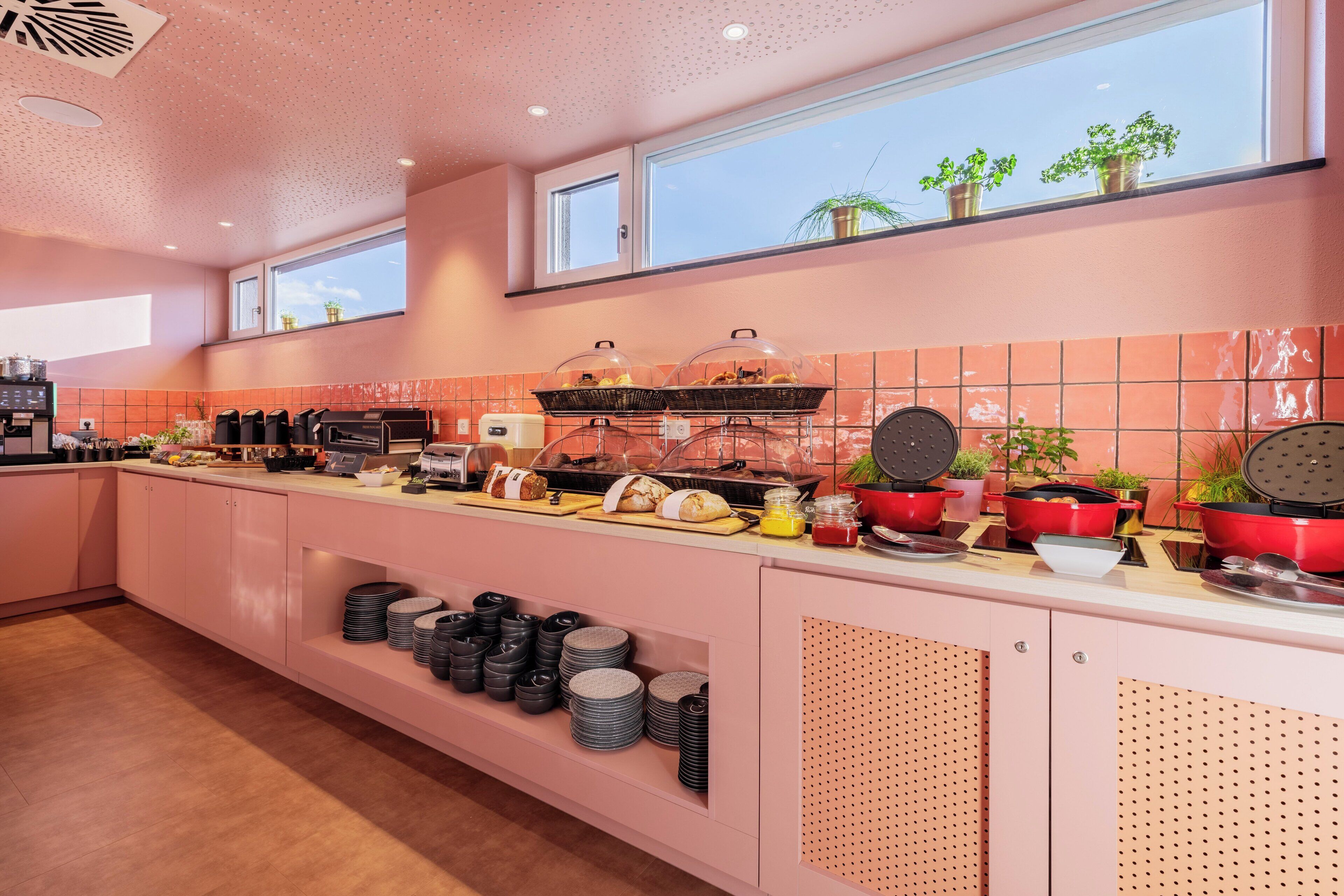 A modern kitchen with pink cabinets, a long counter, and various kitchen appliances.