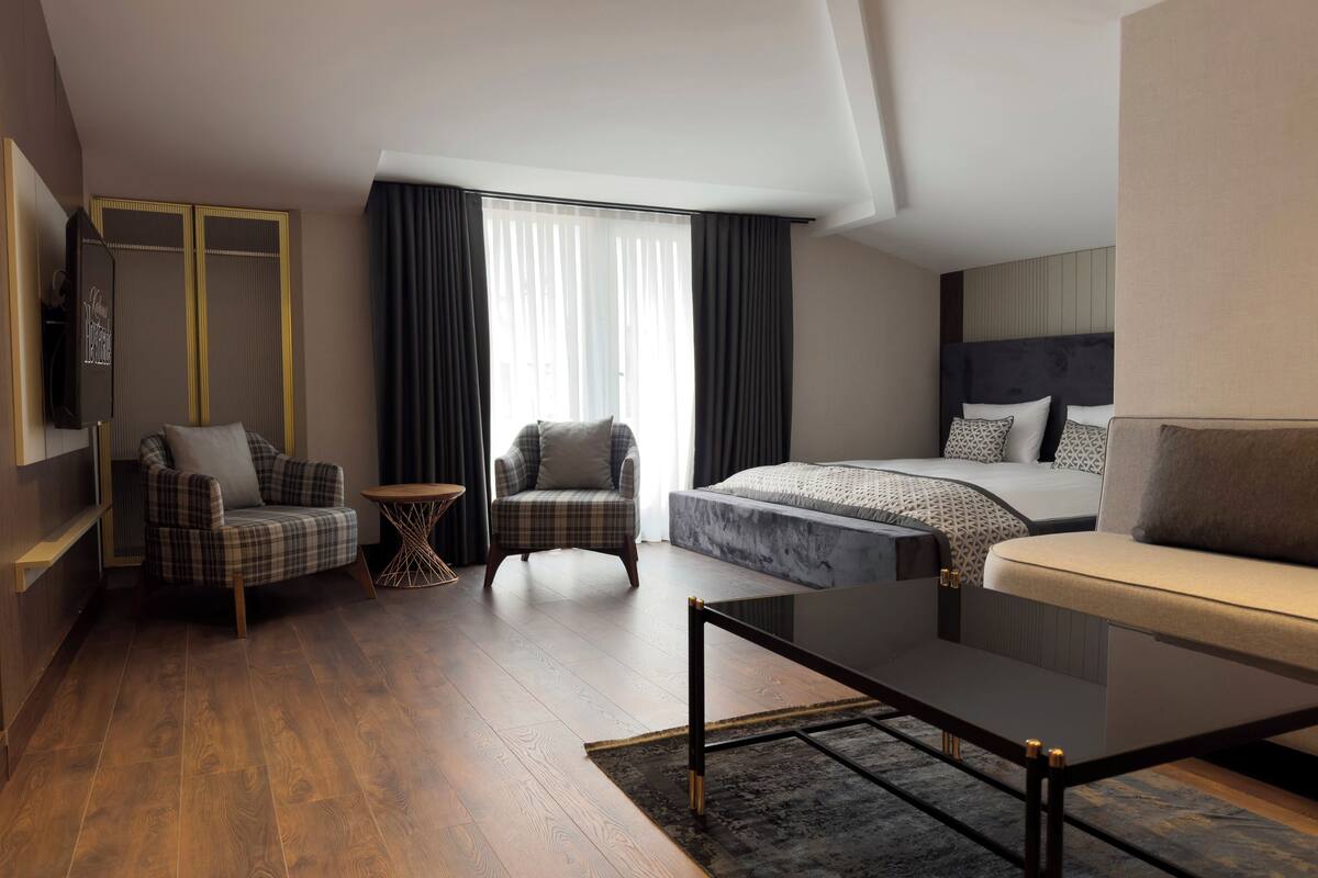 A modern hotel room with a bed, two armchairs, a small table, and a sofa.