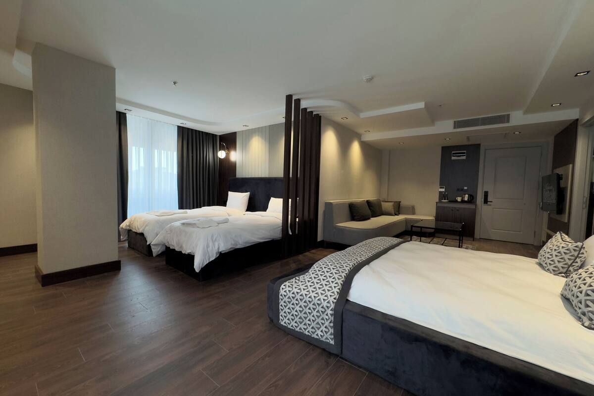 A modern hotel room with two beds, a sofa, and a desk area.