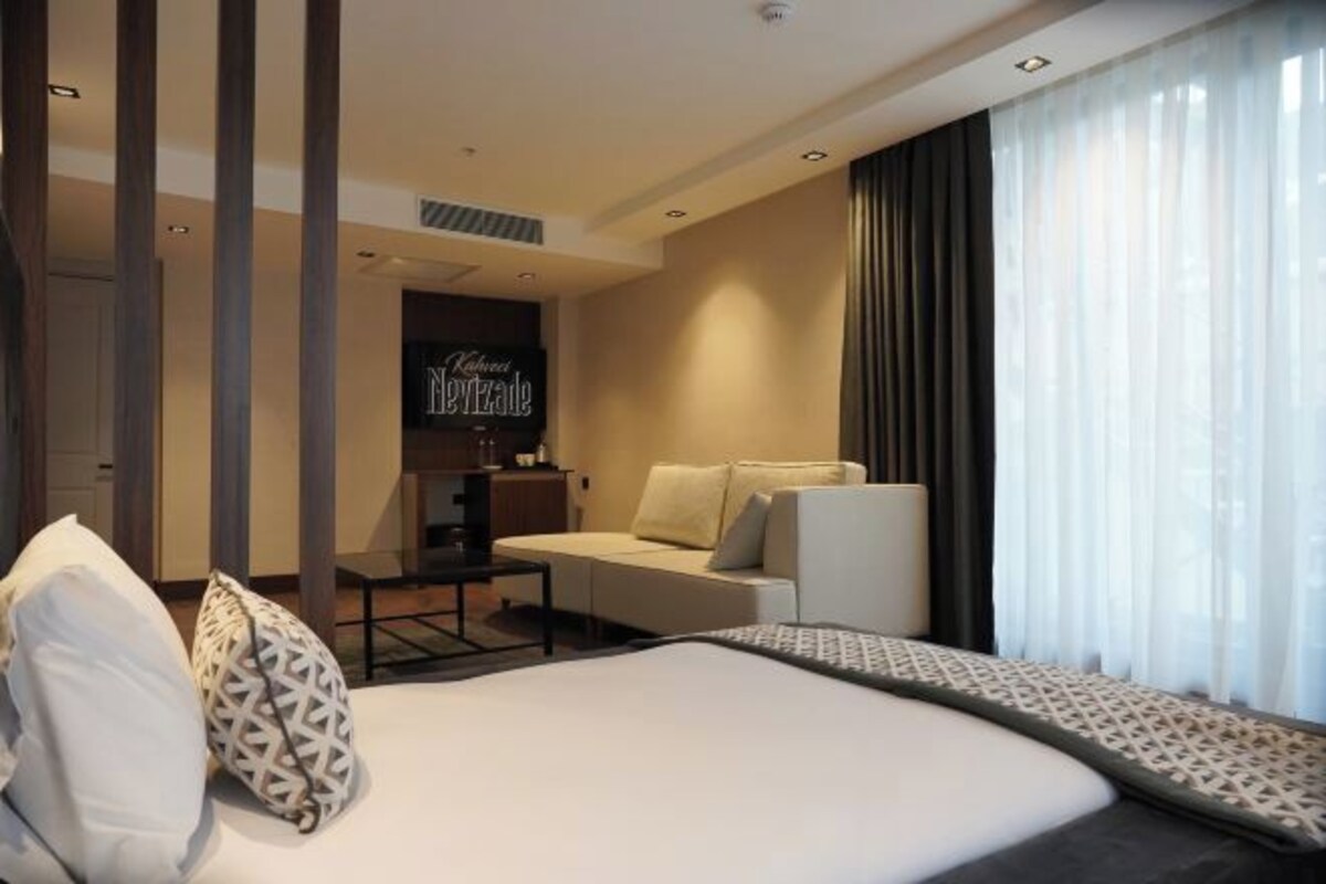 Habitación de hotel con cama, escritorio, silla y un ventanal con cortinas.