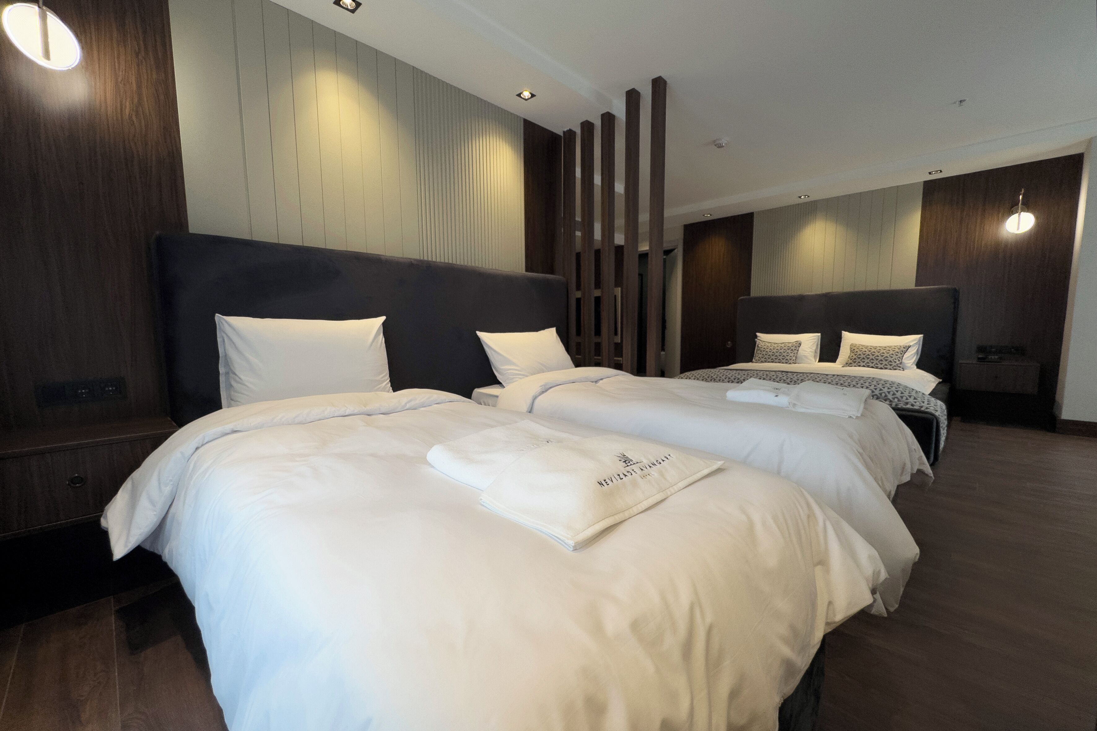 Et moderne hotelværelse med to store senge, en trævæg som detalje og indbygget belysning.