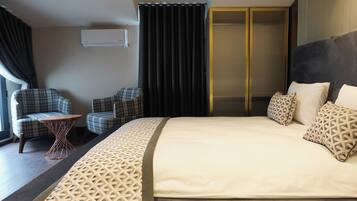 A hotel room with a large bed, two armchairs, a small round table, and a wardrobe.