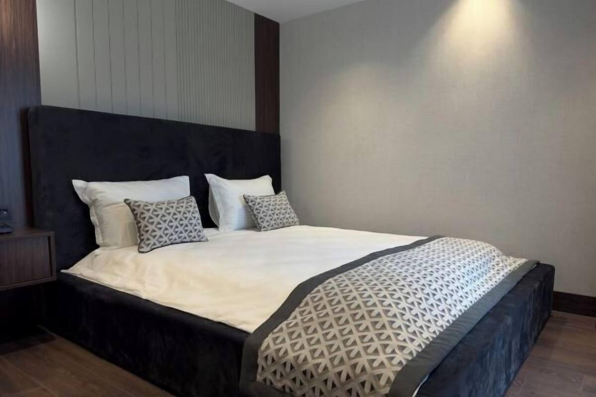 A neatly made bed with a patterned throw, a dark headboard, and a wooden nightstand.