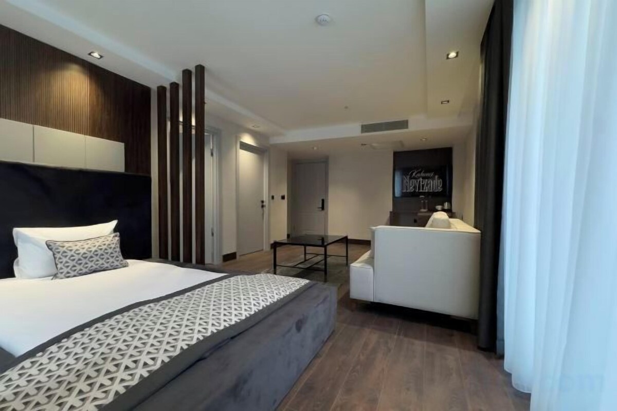 A modern hotel room with a large bed, a separate seating area, and a small kitchenette.