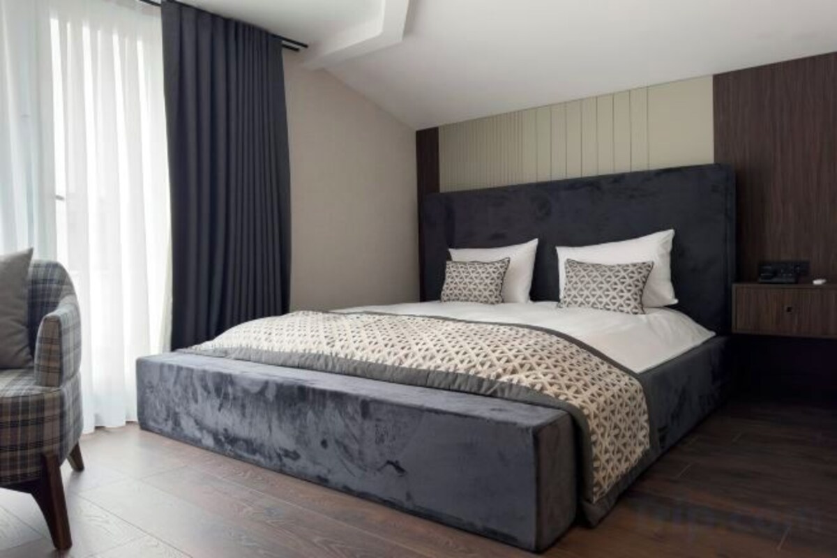 Quarto moderno com uma cama grande, um banquinho, uma cadeira e um guarda-roupa.