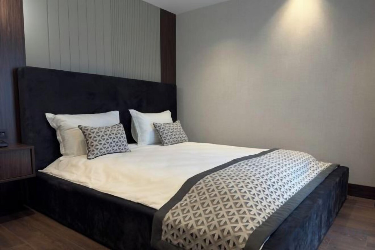 A neatly made bed with a patterned throw, a dark headboard, and a bedside table with a lamp.