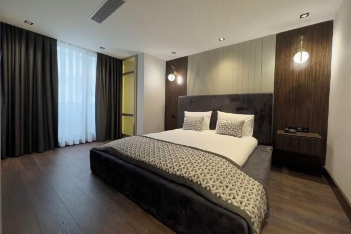 Quarto de hotel moderno com uma cama grande, mesa de cabeceira e vista para o exterior.