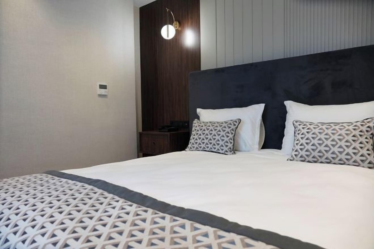 A bedroom with a large bed, a headboard, and a wall-mounted light fixture.