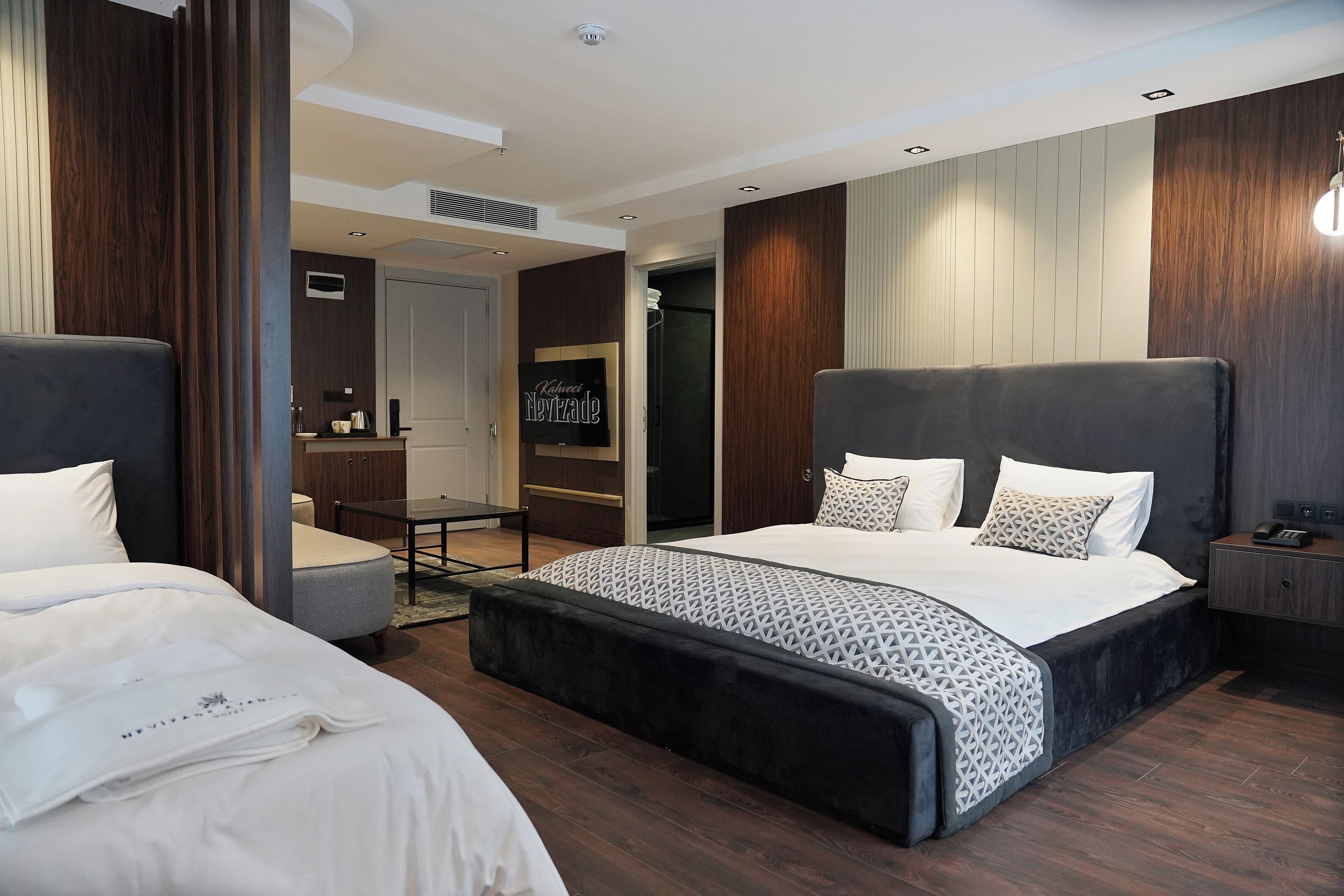A modern hotel room with a large bed, a smaller bed, a desk, and a wardrobe.